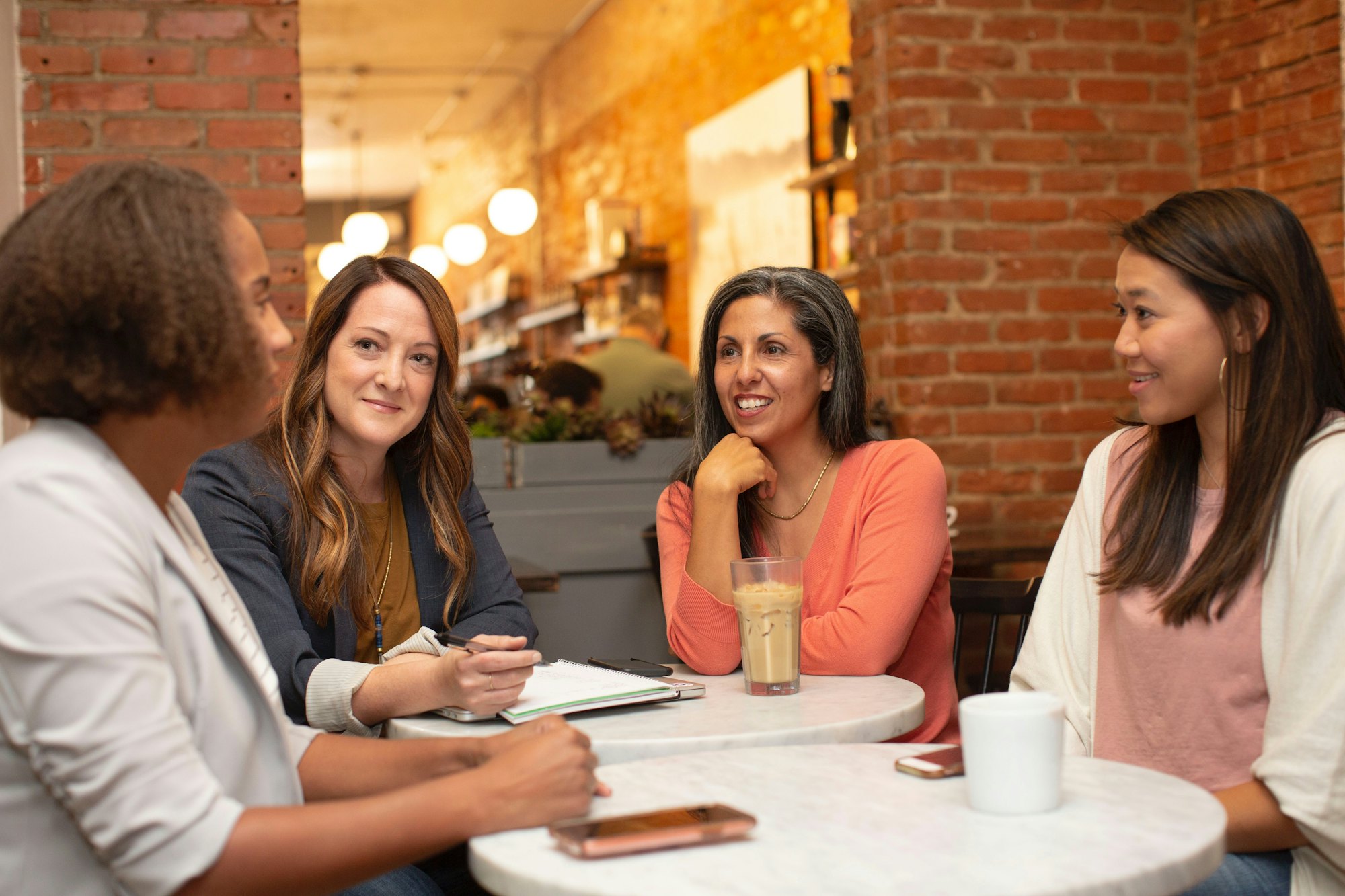 Four women of different backgrounds talking together around a cafe table