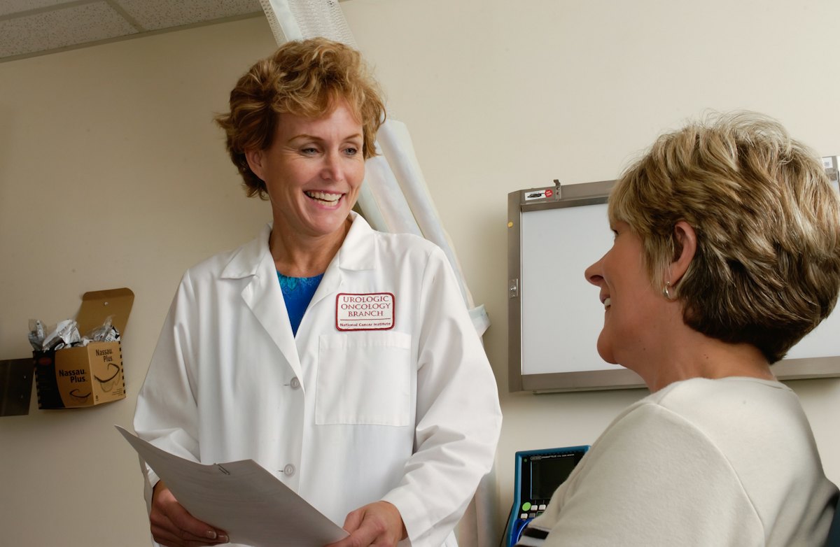 A clinician in a white coat speaking with a patient in a clinic room